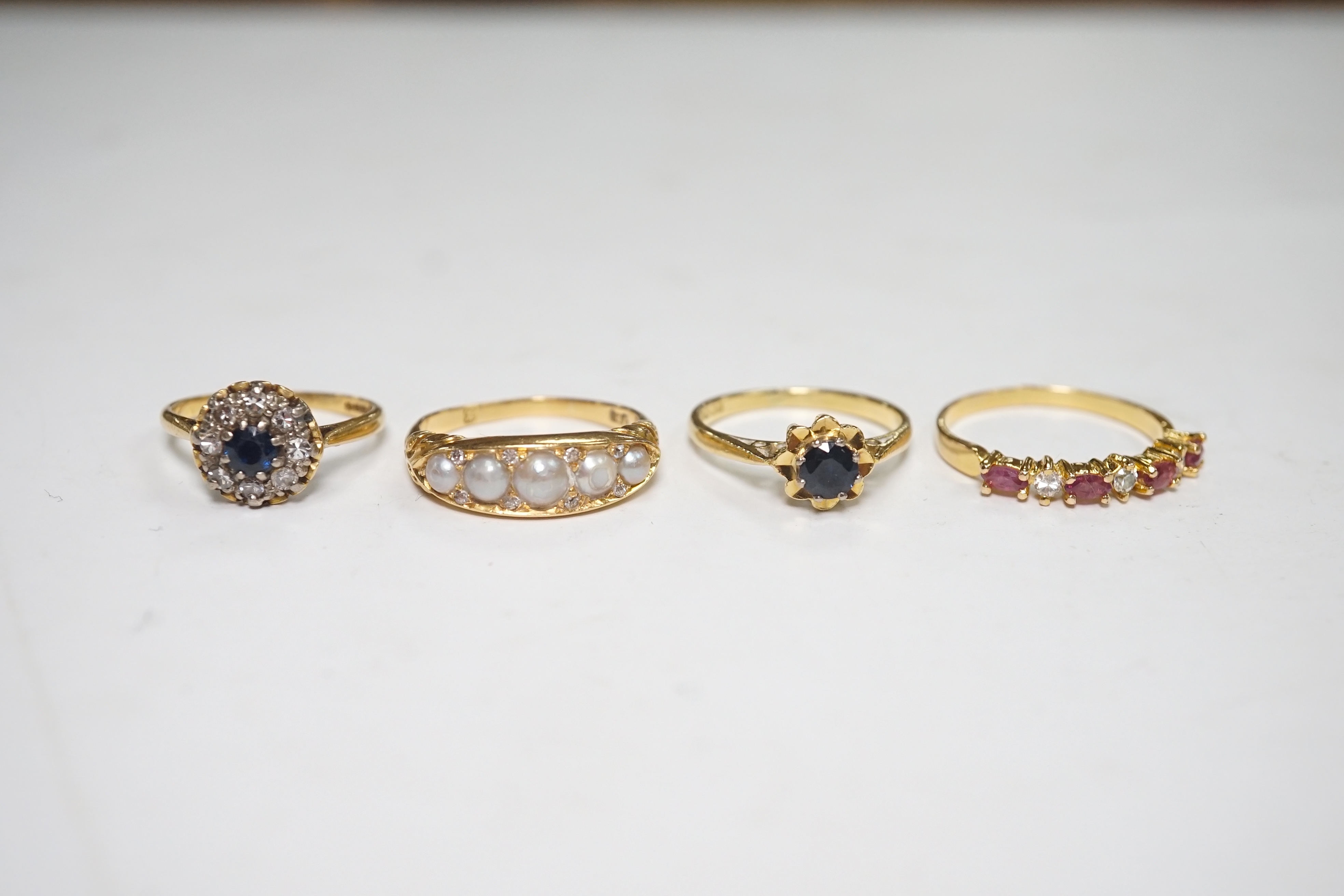 A late Victorian yellow metal and five stone split pearl set half hoop ring, with diamond chip spacers, size N/O, two modern 18ct gold and gem set rings and one other ring. Condition - fair to good